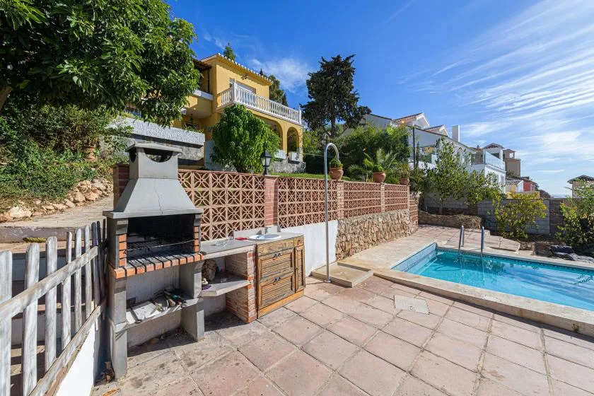 A sunny outdoor patio features a built-in barbecue beside a swimming pool.