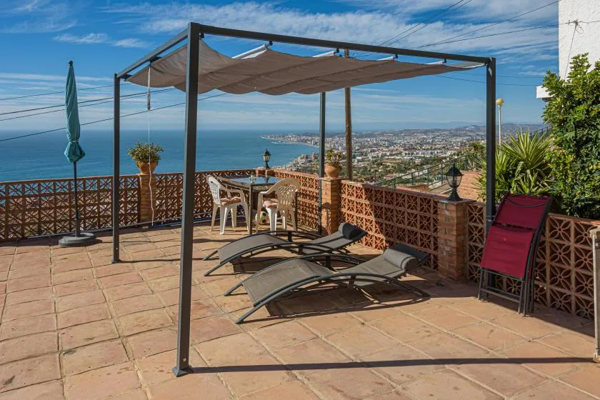 A seaside terrace with a shaded seating area and lounge chairs overlooking the coast.