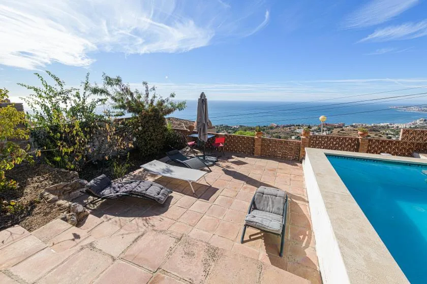 A sunlit patio beside a swimming pool overlooks the ocean.