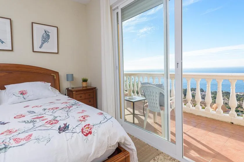 A bedroom with floral bedding opens onto a balcony overlooking the sea.