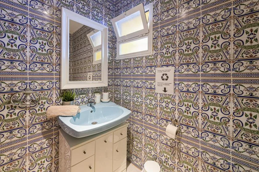 A tiled bathroom with a sink, mirror, and small high windows.