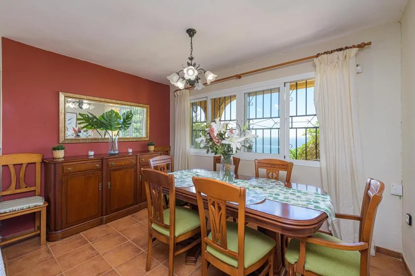 A dining room with a wooden table and chairs beside large windows.