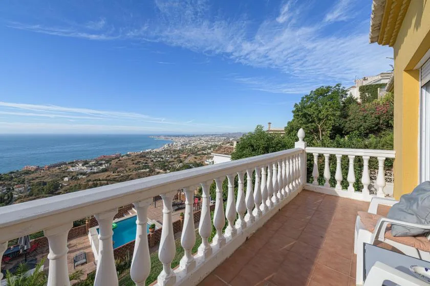 A tiled terrace overlooks the coastline, with a white railing and outdoor seating.