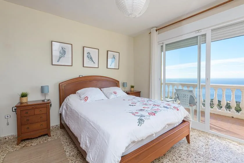 A bedroom with a wooden bed, patterned bedding, and sliding glass doors overlooking the sea.