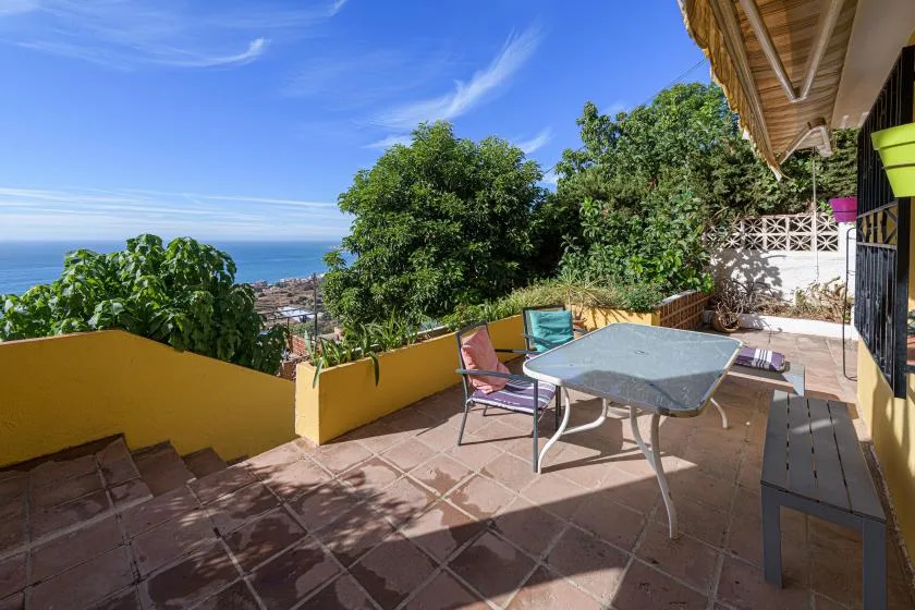 A tiled outdoor terrace with a table and seating overlooks the sea.