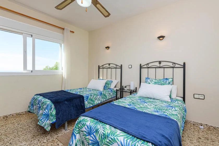 A bright bedroom with two beds dressed in blue and green patterned bedding.