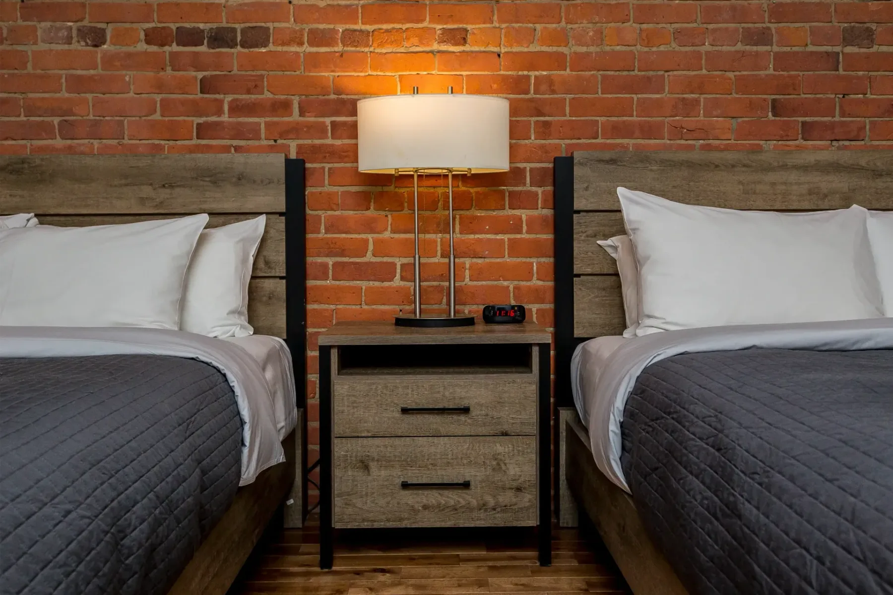 A hotel room with two beds and an exposed brick wall.