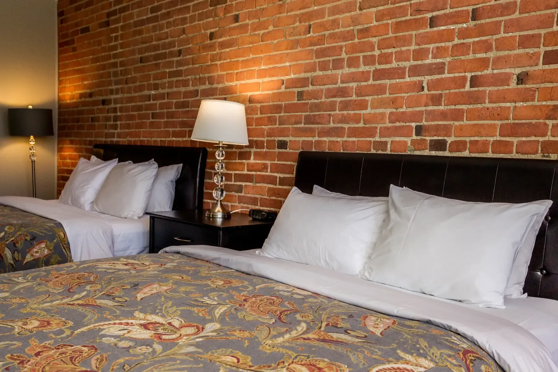 A hotel room with two beds and an exposed brick wall.