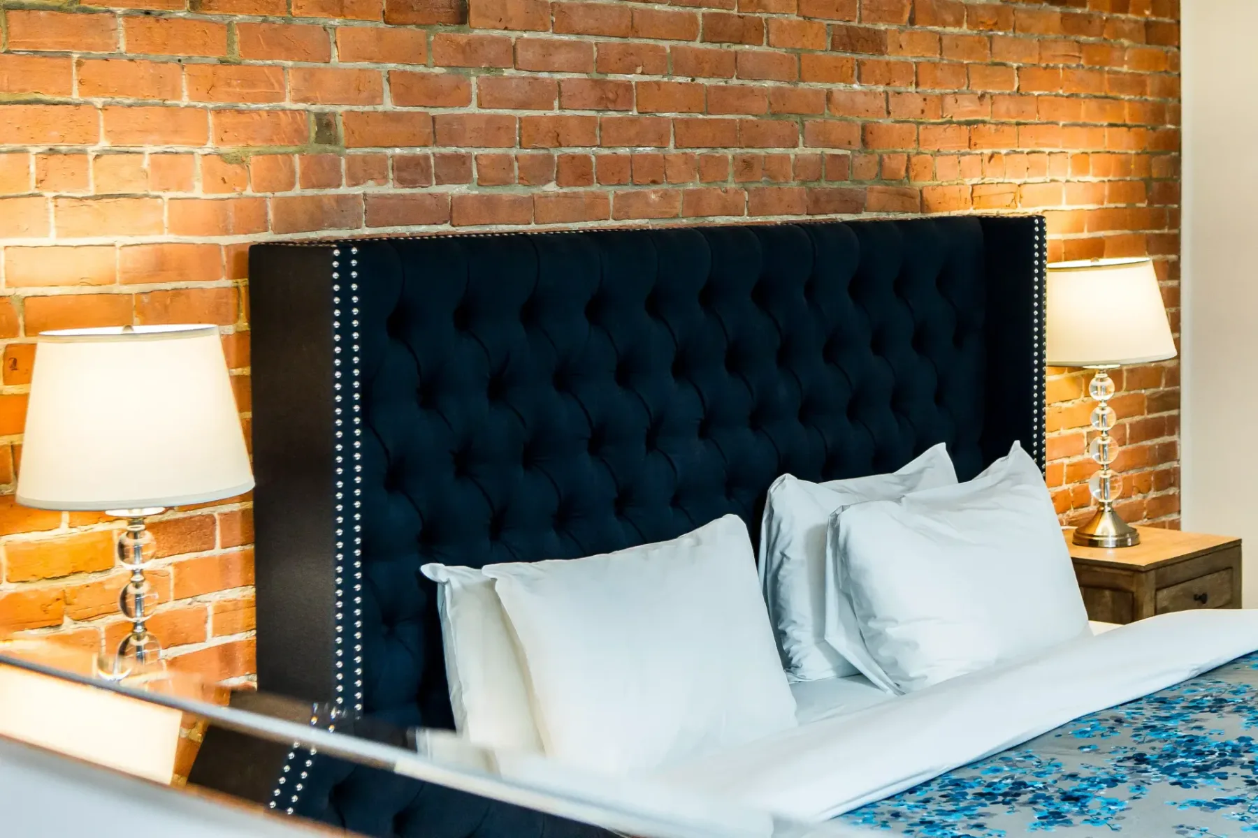 A hotel room with a bed, lamps and exposed brick wall.