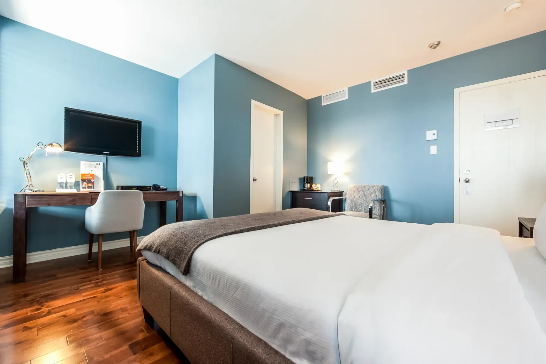 A hotel room with a king-size bed, desk, chair and television.