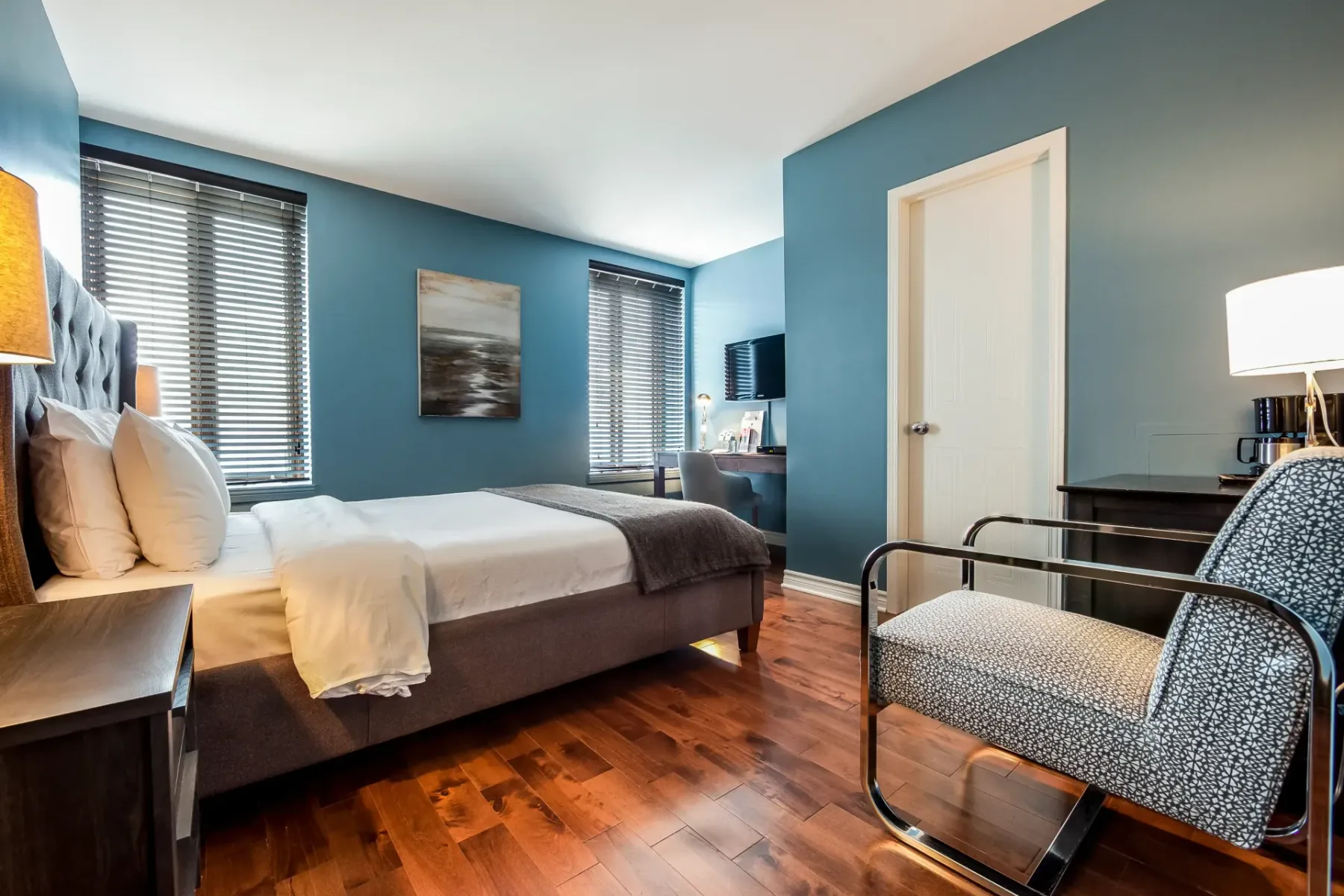 A room with a king-size bed, chair, bedside table and blue walls.
