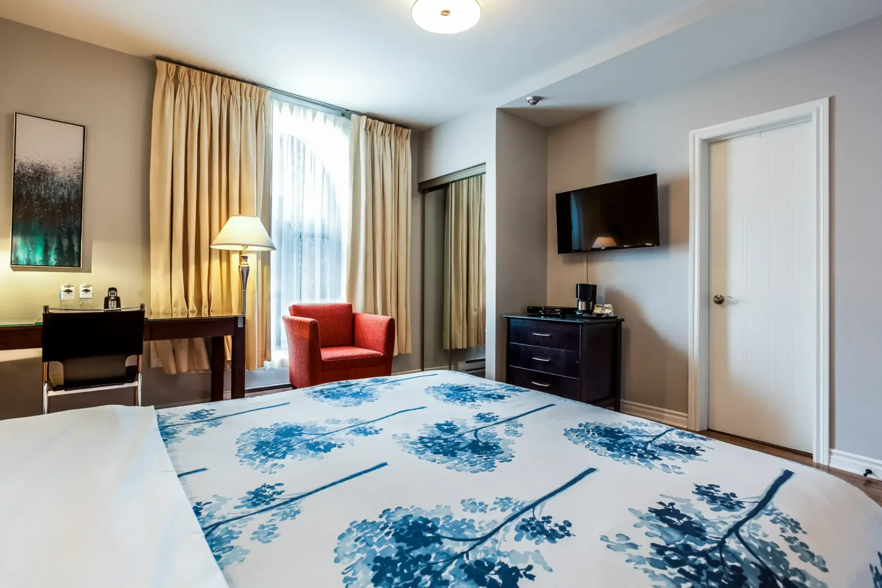 A hotel room with a bed, chair, desk and television.