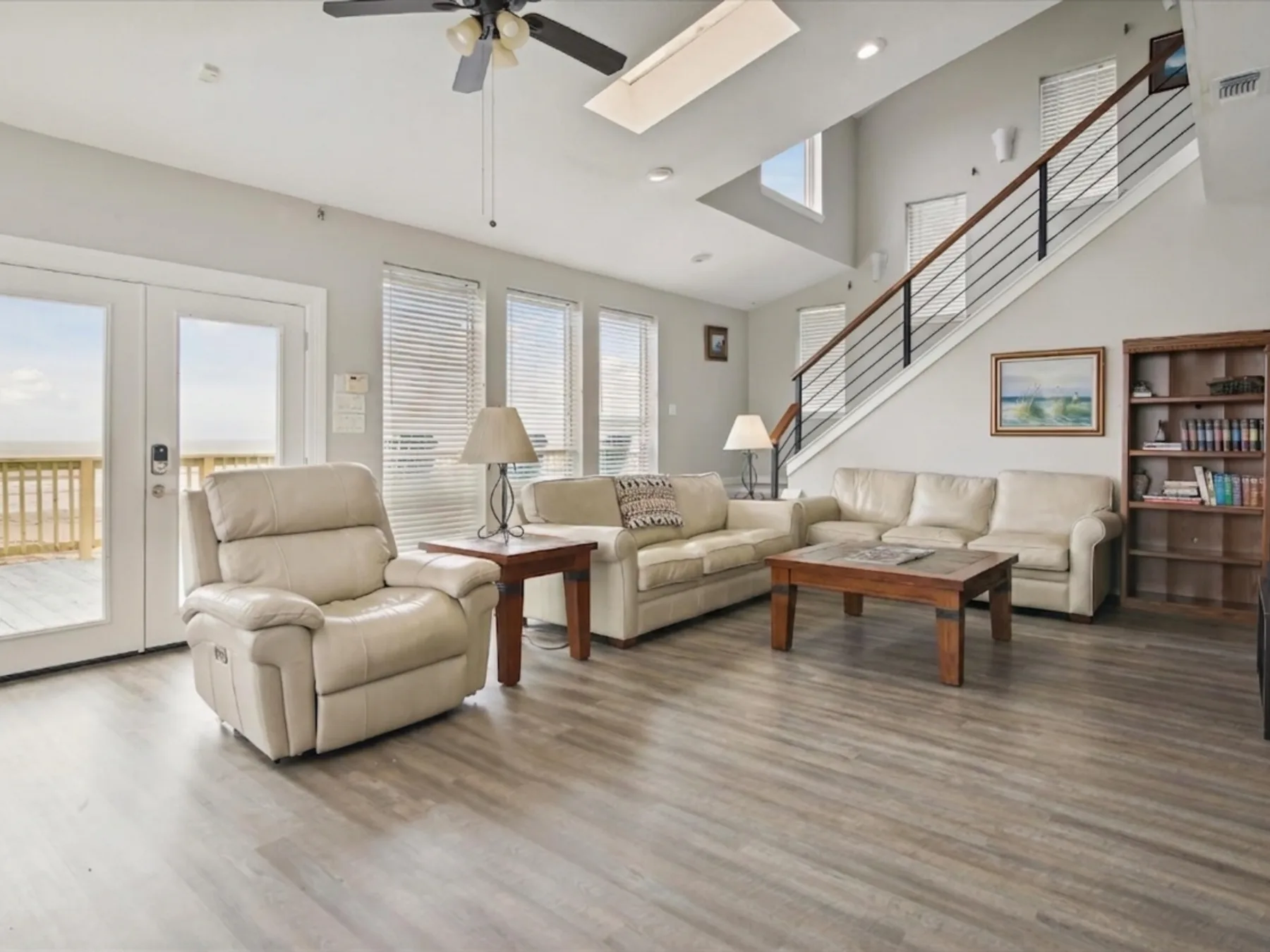 A bright living room with seating, a coffee table, and stairs along the wall.