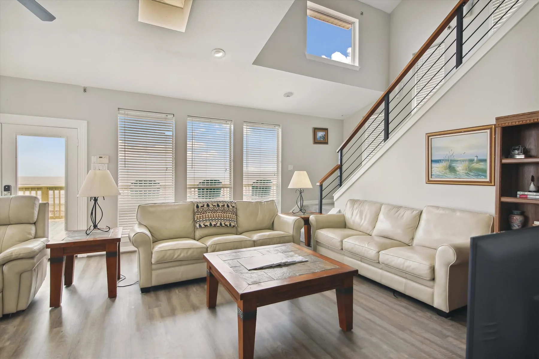 A bright living room has cream seating, a coffee table, and an open staircase.