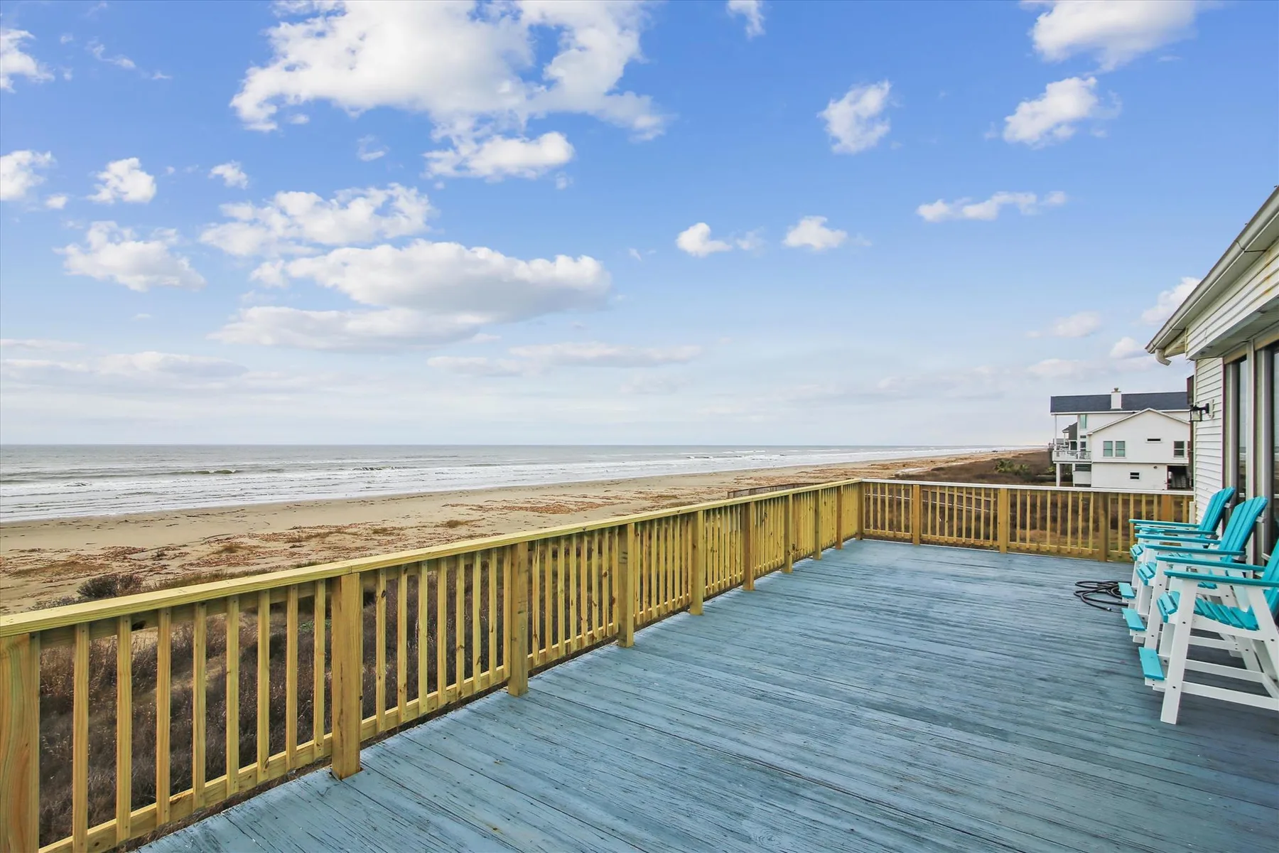 A seaside deck overlooks the beach and ocean, with outdoor seating along the railing.