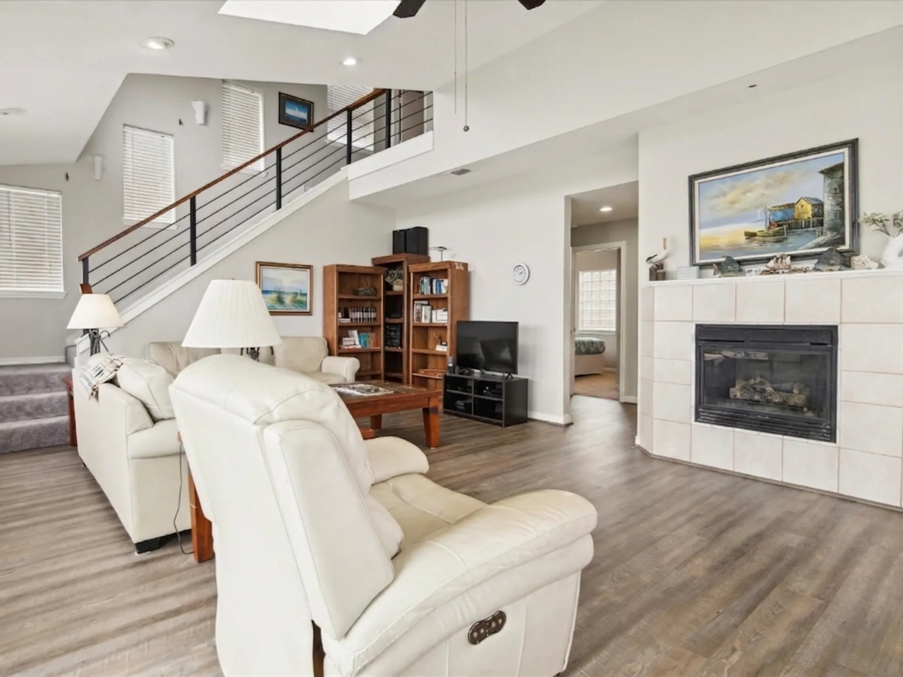 A living room with light-colored seating, a fireplace, and a staircase.
