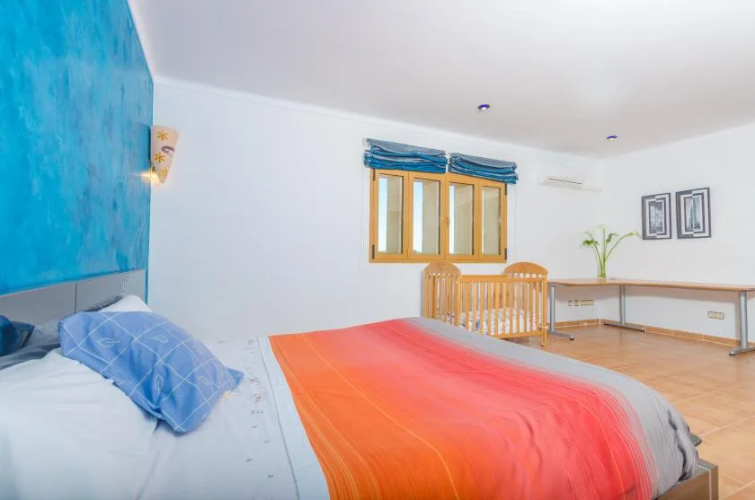 A bedroom with a bed covered by a bright orange blanket and a wooden table.