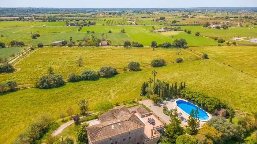 Aerial view of a house with a swimming pool amid open fields.