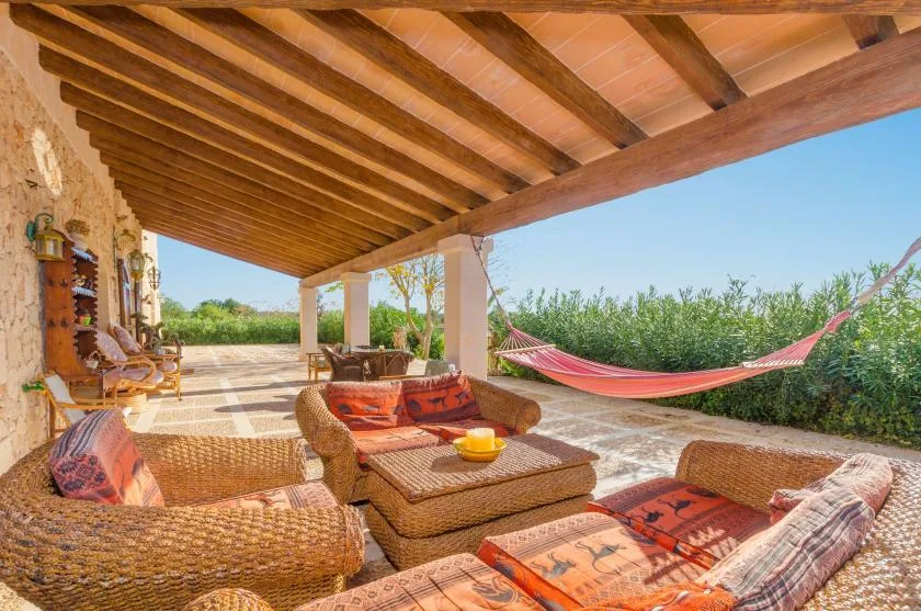 A covered outdoor patio with cushioned seating and a hammock overlooking greenery.