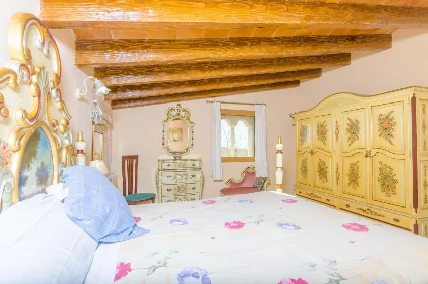 A bedroom with a floral bedspread and ornate wooden ceiling beams.