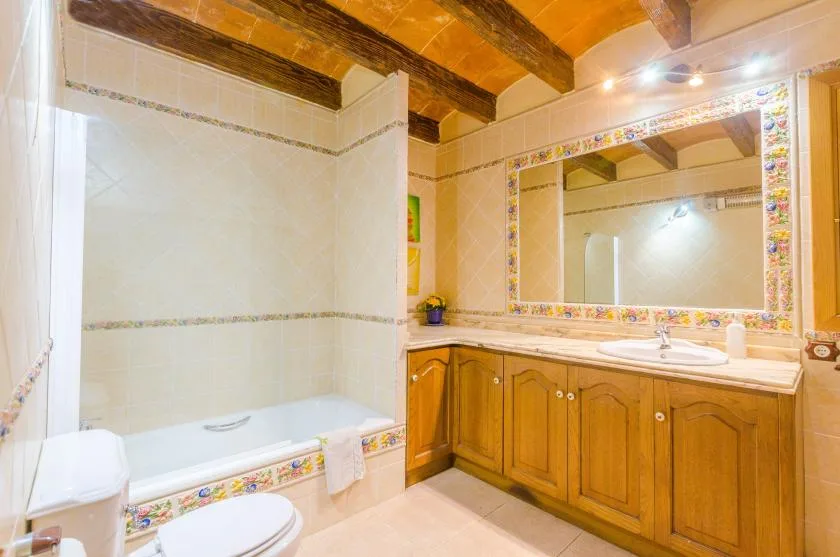 A bathroom with a bathtub, toilet, and wooden vanity beneath a large mirror.