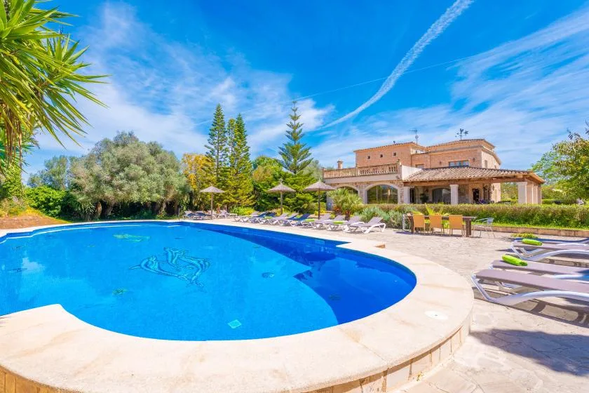 An outdoor swimming pool sits beside a patio with loungers and a building.