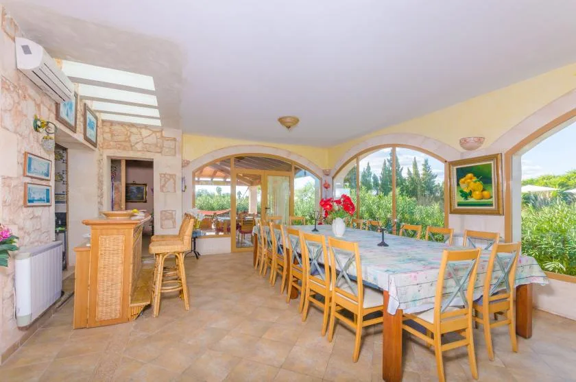 A bright dining room with a long table and large arched windows overlooking greenery.