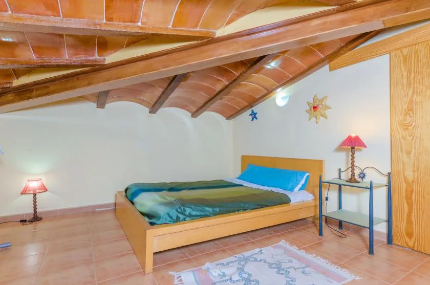 A bedroom with a low bed beneath exposed wooden ceiling beams.