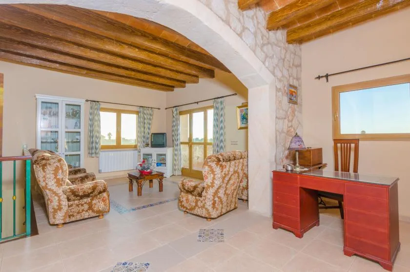 A living room with seating, a small table, and windows beneath exposed wooden beams.