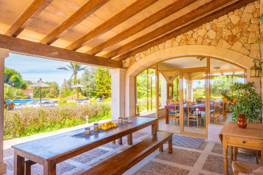 A covered patio with wooden seating overlooks a garden and swimming pool.