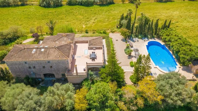 An aerial view shows a stone building beside a swimming pool and green grounds.