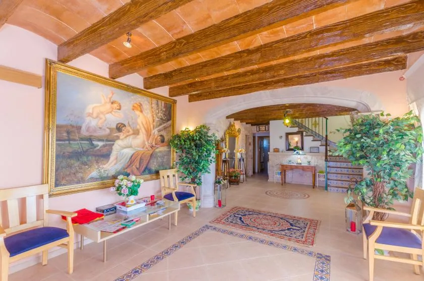 A tiled interior hall with exposed wooden beams, framed artwork, and seating.