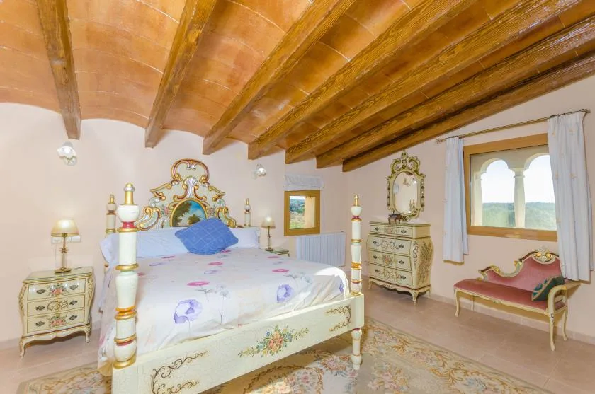 A bedroom with an ornate bed beneath exposed wooden ceiling beams.