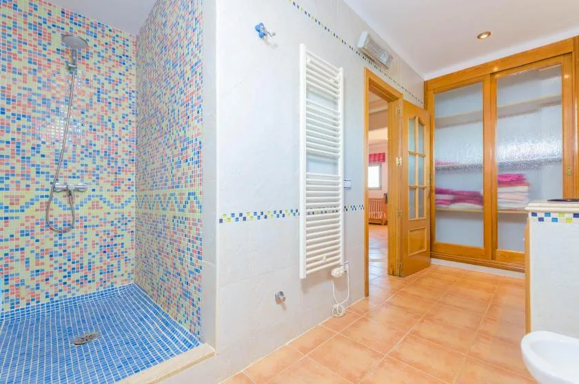 A tiled bathroom with a shower and a wooden storage cabinet.