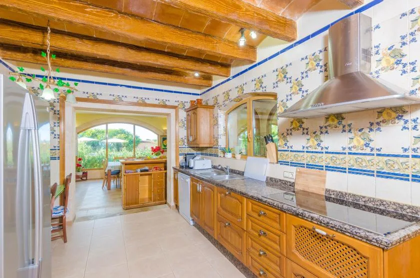 A tiled kitchen with wooden cabinets, a countertop, and a view into a dining area.