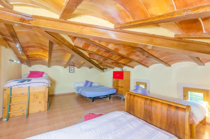 A bedroom with several beds beneath a sloped wooden-beam ceiling.