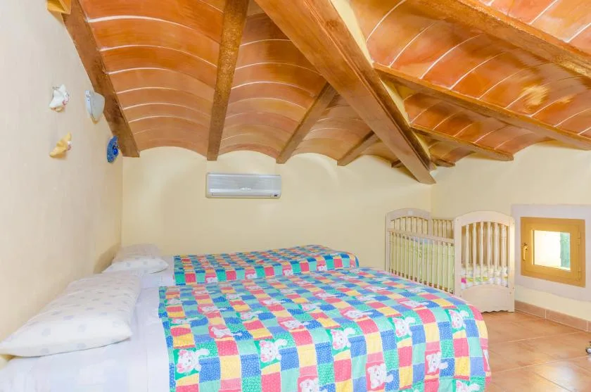 A bedroom with colorful patchwork bedding beneath a sloped wooden ceiling.