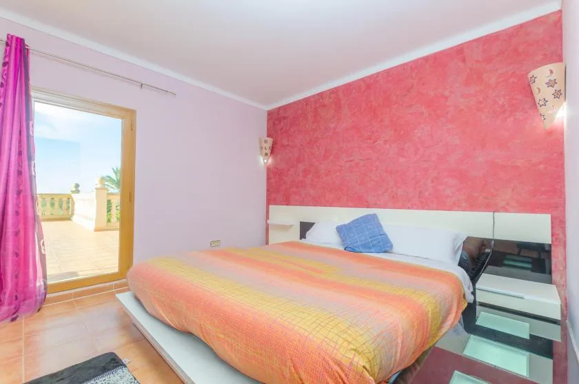 A bedroom with a bed dressed in an orange and pink coverlet.