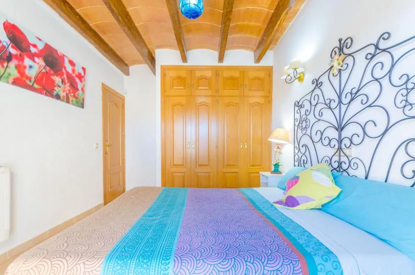 A bedroom with a colorful bedspread and a large wooden wardrobe.