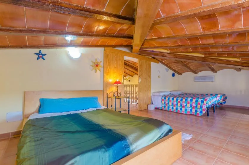 A bedroom with a large bed and a colorful daybed beneath a sloped tiled ceiling.