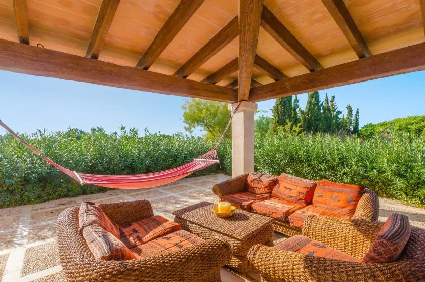 A covered outdoor seating area with cushioned wicker furniture and a hammock.