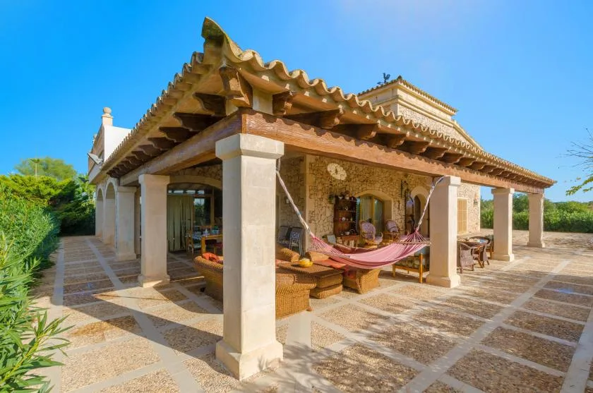 A covered stone patio with a hammock and outdoor seating.