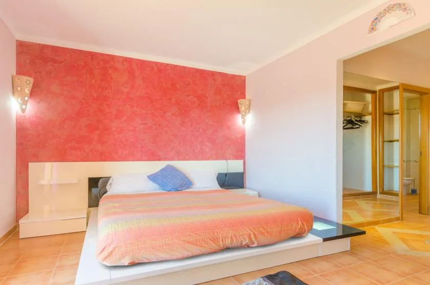 A bedroom with a bed against a coral-colored accent wall.