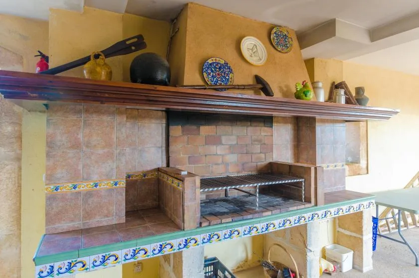 A tiled outdoor grill area with a brick-lined cooking space and decorative dishes above.