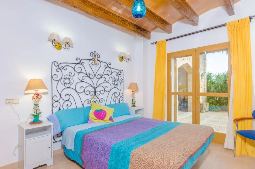 A colorful bedroom with a large bed beside glass doors opening onto a patio.