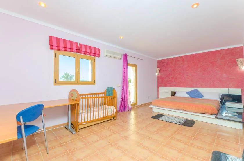 A bedroom with a wooden bed and a crib beside a window.