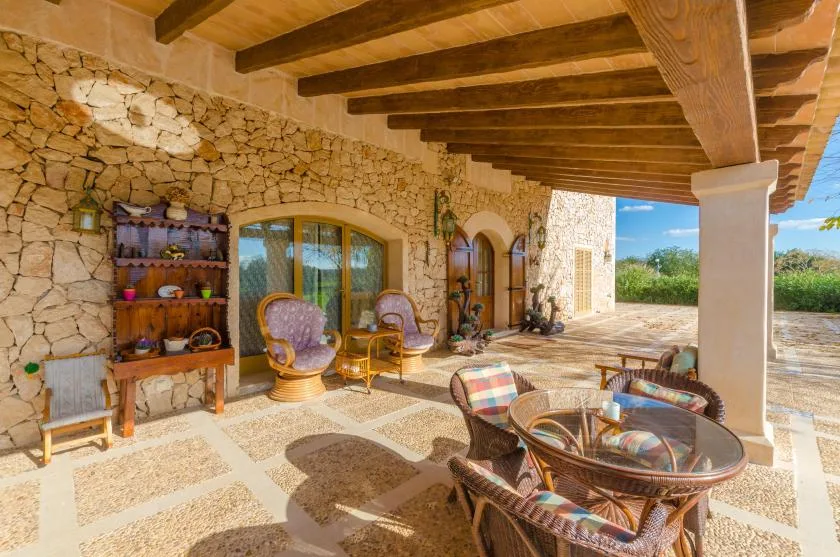 A covered stone patio has wicker seating and a round glass table.