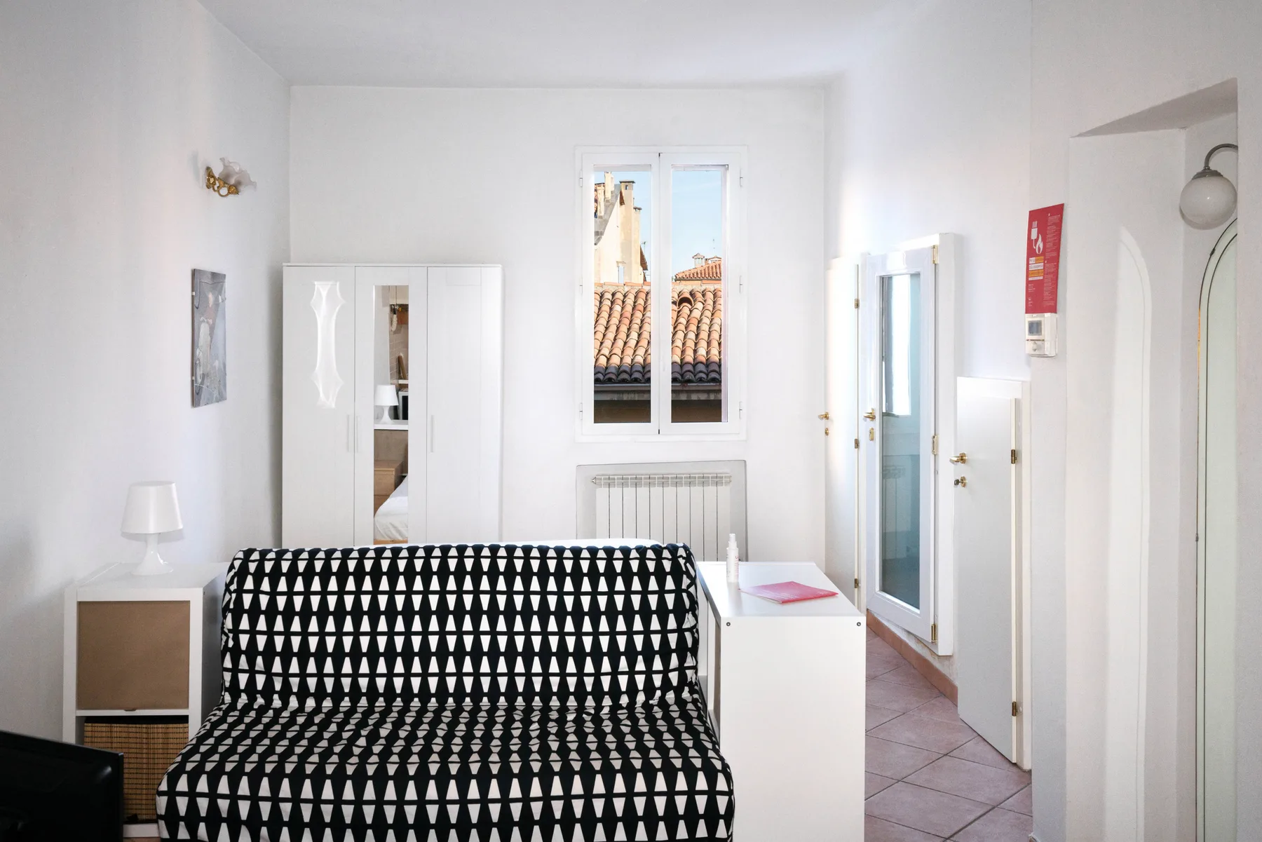 Un dormitorio luminoso con una cama estampada frente a una ventana.