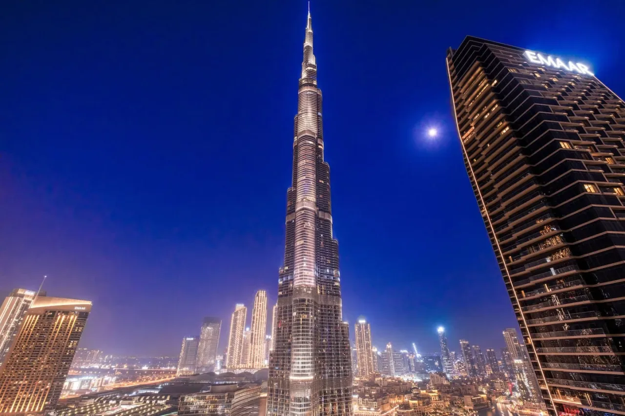 City skyline at night with a very tall illuminated tower and surrounding high-rises.