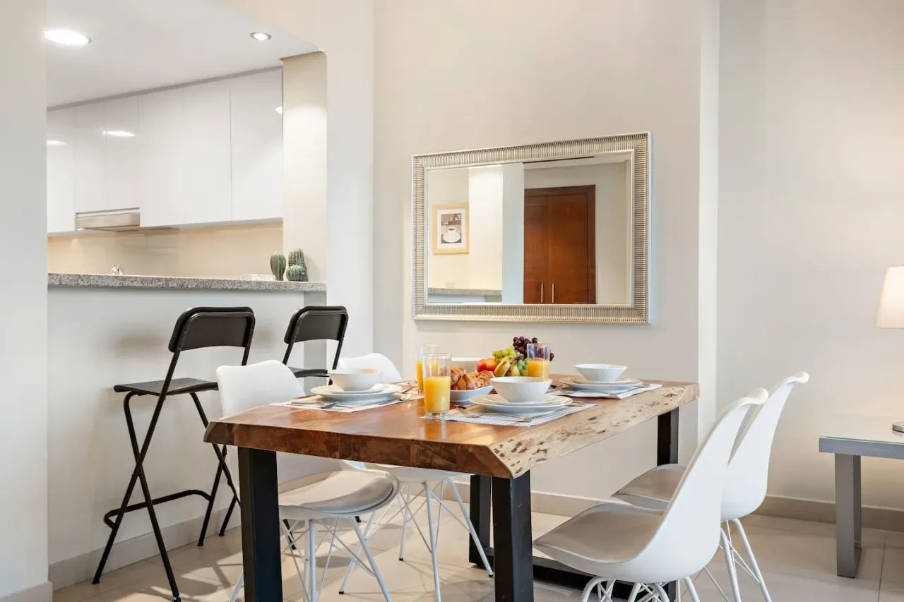 Comedor con una mesa de madera preparada con platos y asientos blancos.